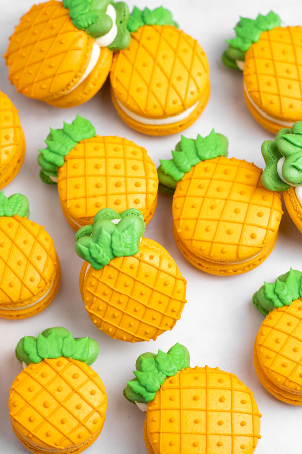 orange and green pineapple macarons scattered on white background