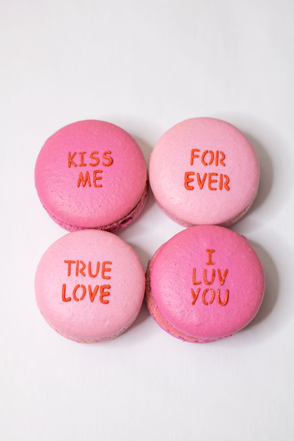 Four light and dark pink conversation heart macarons on white background