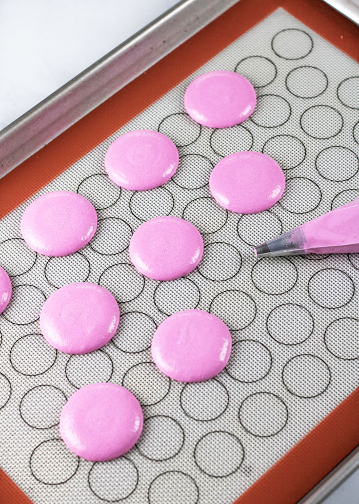 piped pink macaron on baking tray with pastry bag
