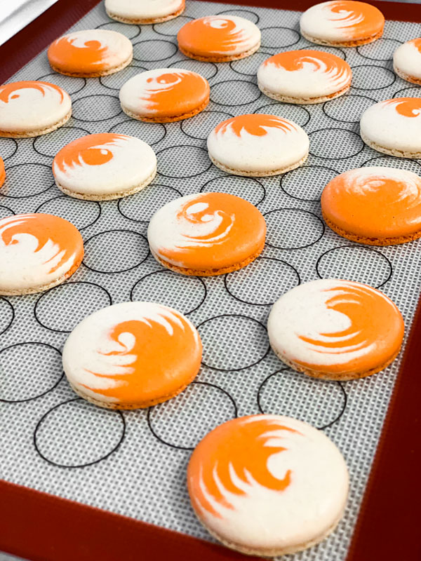 orange and white swirled pumpkin cheesecake macaron shells on baking mat