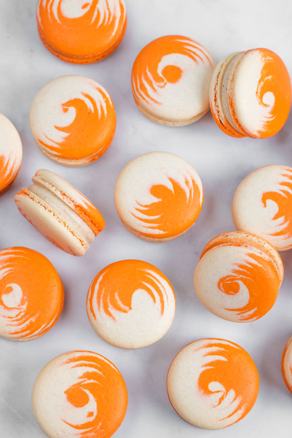 orange and white swirled pumpkin cheesecake macarons on white background