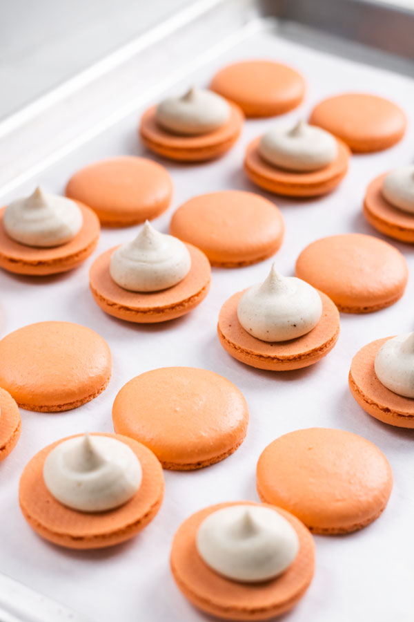 Orange pumpkin spice macarons with pumpkin spice buttercream on parchment paper