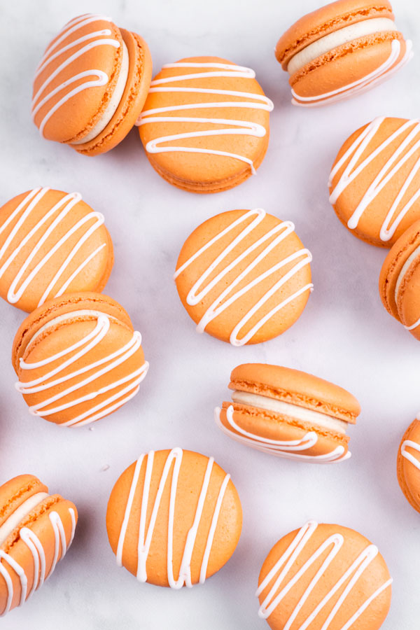Orange pumpkin spice macarons with white drizzle on white background