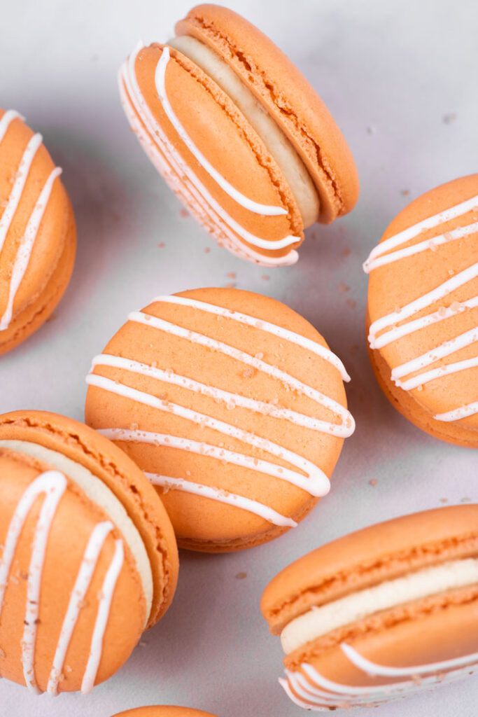 closeup of orange salted caramel macarons with white drizzle and salt