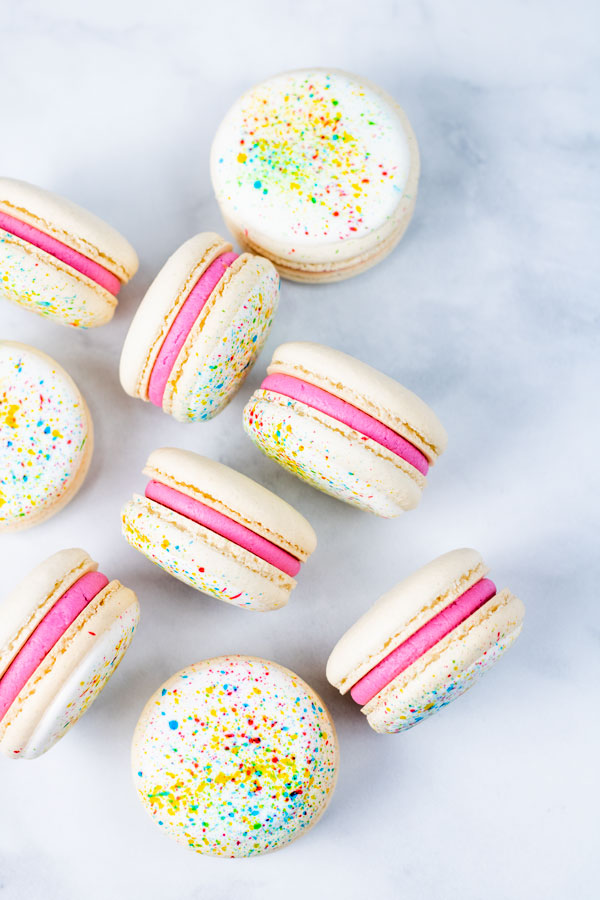 group of splatter paint macarons with pink buttercream on white background