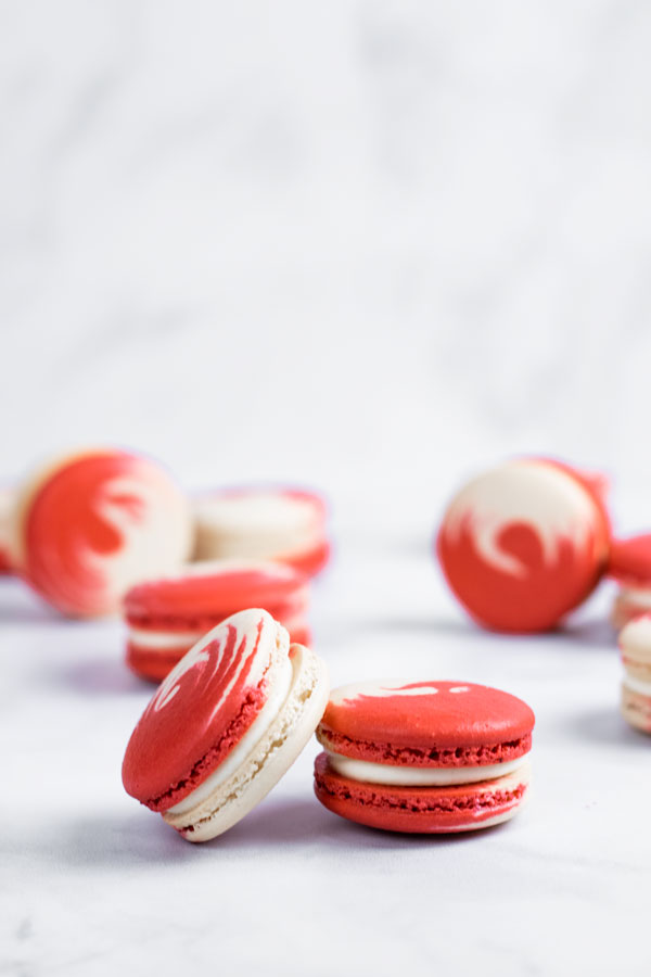two red and white swirled strawberry cheesecake macarons in front of macarons