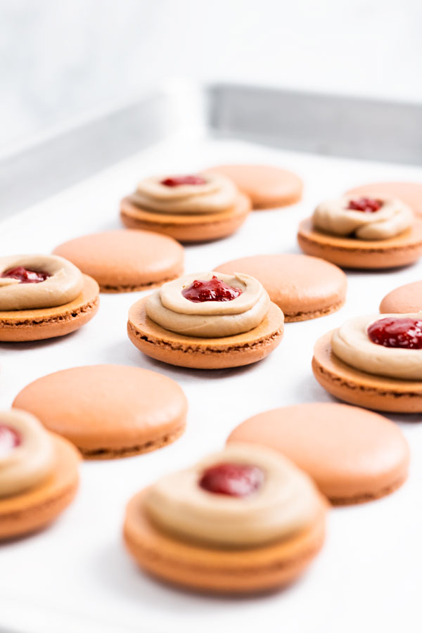 chocolate macaron shells with choclate buttercream and strawberry jam on baking sheet