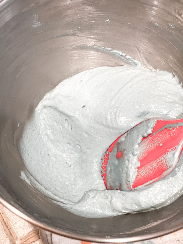 blue macaron batter and red spatula in mixing bowl