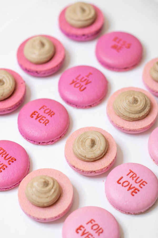 Light and dark pink conversation heart macaron shells with chocolate buttercream