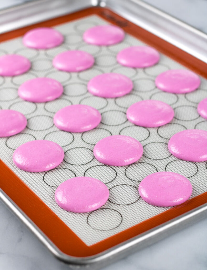 piped pink macarons on baking tray
